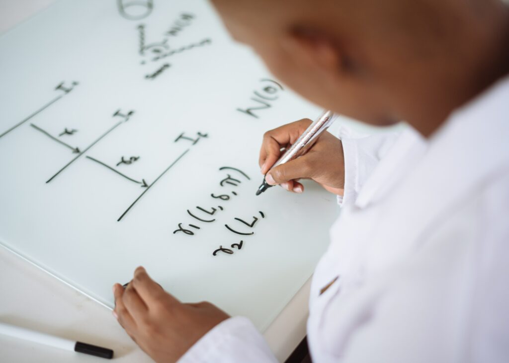 étudiant en blouse blanche, qui écrit une formule mathématique sur un tableau blanc